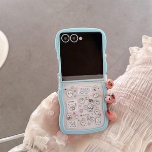 May include: A light blue phone case with a clear, patterned section featuring cartoon animal stickers. The case is open, revealing a black screen. The case has a rounded design and is held by a person.