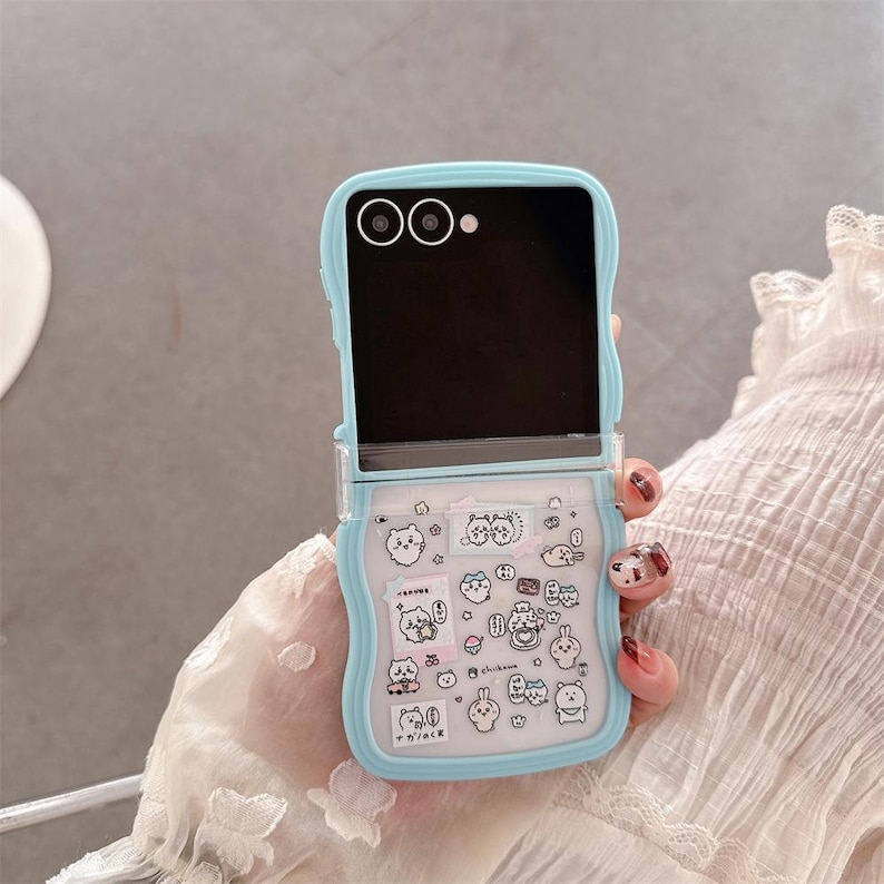 May include: A light blue phone case with a clear, patterned section featuring cartoon animal stickers. The case is open, revealing a black screen. The case has a rounded design and is held by a person.