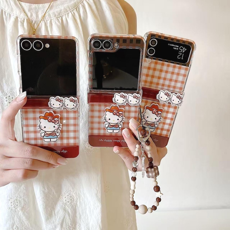 Op de afbeelding: Transparante telefoonhoesjes met een rood-wit ruitpatroon en een Hello Kitty-ontwerp. De hoesjes hebben een rode rand en een Hello Kitty-bedel. De hoesjes zijn open en tonen de schermen van de telefoons.