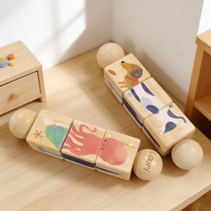 May include: Wooden toy blocks with animal illustrations, including a dog, octopus, and turtle. The blocks are connected with wooden spheres. The word "lauri" is printed on one of the spheres. The blocks are arranged on a light-colored wooden surface.