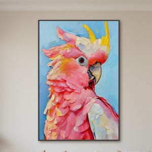 Op de afbeelding: Een ingelijst schilderij van een roze en gele papegaai tegen een lichtblauwe achtergrond. De papegaai is afgebeeld in een textuurrijke, impressionistische stijl, met zichtbare penseelstreken. Het kunstwerk wordt boven een witte bank getoond.