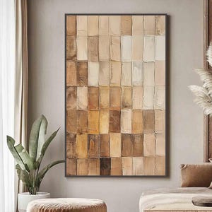 May include: Abstract wall art with a rectangular design of textured, vertical blocks in shades of brown, beige, and cream. The artwork is framed in a dark brown border, suitable for interior decor. The artwork is displayed in a living room setting.