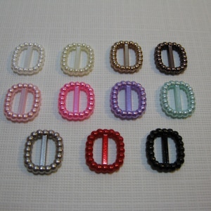 May include: Twelve different colored plastic buckles with a pearl-like finish. Each buckle is oval shaped and has a center bar.