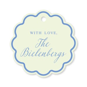 May include: A scalloped-edge gift tag with a pale yellow background and a blue border. The text "WITH LOVE, The Bielenberg's" is written in blue script. A small hole is at the top for attaching the tag.