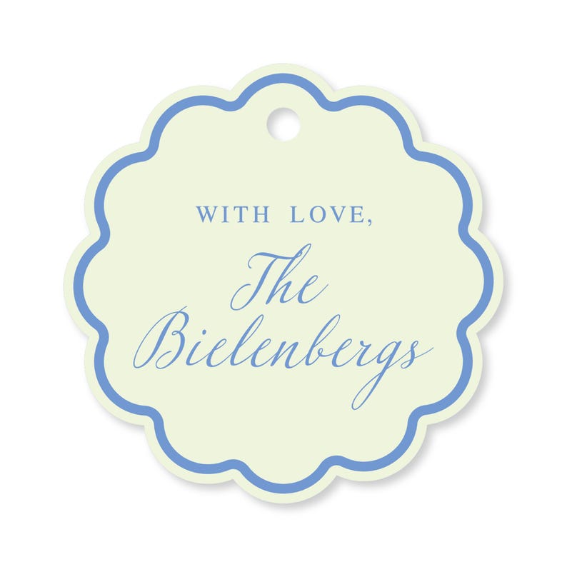 May include: A scalloped-edge gift tag with a pale yellow background and a blue border. The text "WITH LOVE, The Bielenberg's" is written in blue script. A small hole is at the top for attaching the tag.