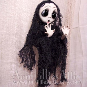 May include: A handmade ghost doll with large eyes and a distressed black fabric dress. The doll is hanging from a string and has a surprised expression.