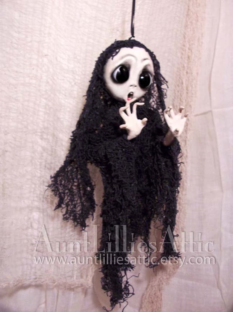 May include: A handmade ghost doll with large eyes and a distressed black fabric dress. The doll is hanging from a string and has a surprised expression.