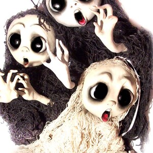 May include: Three handmade dolls with large eyes and open mouths, each wearing a different type of fabric. The dolls are made of white fabric and have painted features. The dolls are dressed in white, black, and brown fabric.
