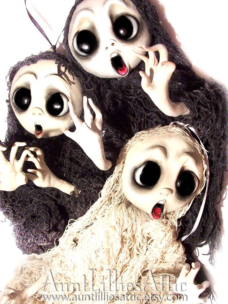 May include: Three handmade dolls with large eyes and open mouths, each wearing a different type of fabric. The dolls are made of white fabric and have painted features. The dolls are dressed in white, black, and brown fabric.