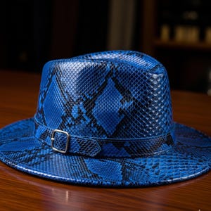 Può includere: Un cappello fedora blu con motivo a pelle di serpente. Il cappello presenta una fibbia color argento su una fascia che avvolge la corona. Realizzato in materiale strutturato, è appoggiato su una superficie di legno.