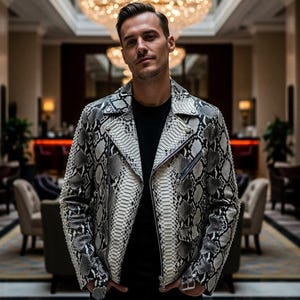 Może przedstawiać: Czarna i biała skórzana kurtka ze wzorem skóry węża, zapinana na zamek błyskawiczny. Kurtka ma klasyczny styl motocyklowy z wykładanym kołnierzem i wieloma kieszeniami. Noszona na czarnej koszulce.