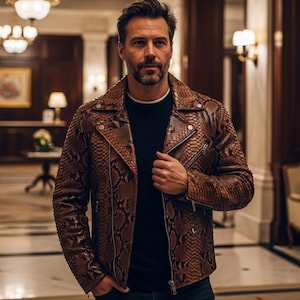 May include: A brown snakeskin-effect leather jacket with a zip closure and pockets. The jacket is worn over a black top. The background shows a hallway with decorative lighting and a painting.