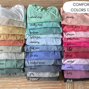 A collection of various colored t-shirts neatly stacked on top of each other, with each color labeled.