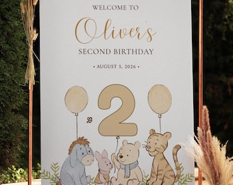May include: A sign for a second birthday celebration, featuring the text "Welcome to Oliver's Second Birthday" and the date August 5, 2026. The sign includes illustrations of cartoon characters, balloons, and the number 2. The sign is displayed on a copper-colored metal stand.