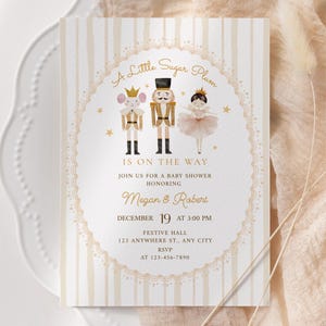 May include: A rectangular baby shower invitation card with a beige striped background and a central oval frame. It features illustrations of a mouse, a nutcracker, and a ballerina, with gold text reading A Little Sugar Plum IS ON THE WAY.