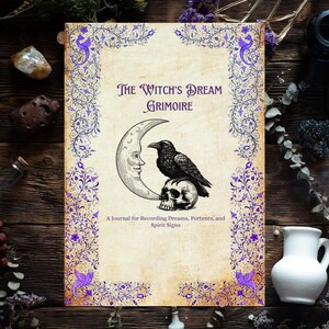 May include: A grimoire with the title "The Witch's Dream" and a raven perched on a skull in front of a crescent moon. The cover has a floral border in purple. The journal is on a wooden surface.