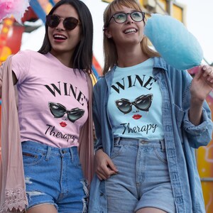 two ladies wearing retro wine therapy tshirt with large cat eye sunglasses Wine Therapy Bella TShirt Retro Cat Eye Sunglasses Funny Wine Lover Tee Wine Mom Shirt Wine Gift for Her Vintage Wine Glamour Sunglasses Tee eating cotton candy at the fair