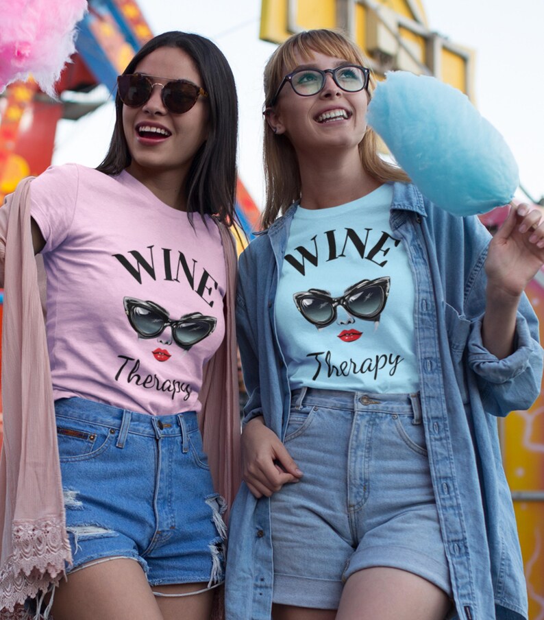 two ladies wearing retro wine therapy tshirt with large cat eye sunglasses Wine Therapy Bella TShirt Retro Cat Eye Sunglasses Funny Wine Lover Tee Wine Mom Shirt Wine Gift for Her Vintage Wine Glamour Sunglasses Tee eating cotton candy at the fair