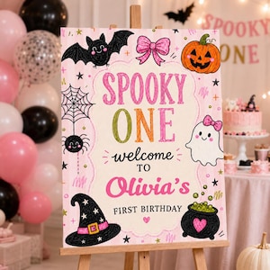 May include: A rectangular sign with a light pink striped background featuring Halloween illustrations including a black bat, a pink bow, an orange pumpkin, a spider web, a spider, a white ghost with a pink bow, a witch hat, and a black cauldron.