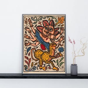 May include: A framed folk art print depicting a multi-armed deity with a cat-like face riding a tiger-like creature. The artwork uses bright colours and detailed linework. The background is beige, and the frame is black.