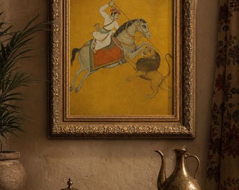 May include: A framed painting featuring a person in white traditional attire riding a grey horse and wielding a spear against a lion, set against a mustard yellow background. The artwork is enclosed in an ornate, textured gold-coloured frame.