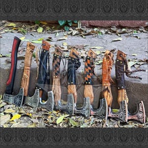 May include: A collection of Viking axes with wooden handles and intricately designed metal axe heads. The handles are wrapped in leather and rope, with various colors and patterns. The axes are displayed outdoors.