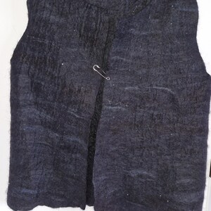 May include: A dark grey felt vest with a textured surface, fastened with a silver safety pin. The sleeveless vest has a rounded neckline. The brand name "knitonefelt two" is visible on the label.