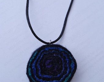 Ciondolo a spirale in feltro realizzato a mano in seta di gelso e lana tinte a mano nei colori viola, indaco, blu e verde, con collana in cordino di raso nero.