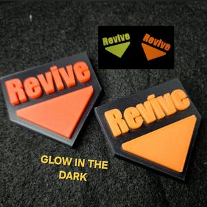 May include: Two black, geometric-shaped badges with the word "Revive" in orange, raised lettering and an orange triangle. The text "Glow in the Dark" is below the badges. A smaller image shows the badges glowing.
