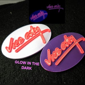 May include: Oval-shaped Vice City logo in red on white and purple backgrounds. The text "Vice City" is in a stylized font, with a red X crossing through the words. The image includes a smaller, glowing version of the logo. The text "Glow in the Dark" is also present.