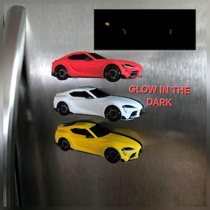 May include: Three sports car magnets in red, white, and yellow, each featuring black wheels and windows. The text GLOW IN THE DARK is printed in red next to the cars, with a small inset box showing the cars illuminated in the dark.