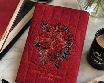May include: A rectangular, quilted red fabric notebook cover featuring an embroidered design of a central anatomical heart surrounded by roses and skulls. The text "People & Paperwork New York" is embroidered in red thread near the bottom edge.