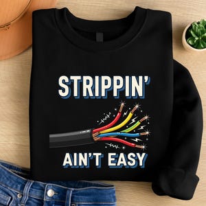 Op de afbeelding: Zwart sweatshirt met de tekst "STRIPPIN' AIN'T EASY" in witte en blauwe letters. Een afbeelding van een gestripte elektrische kabel met rode, gele, blauwe en groene draden staat eronder. De sweatshirt heeft een ronde hals.