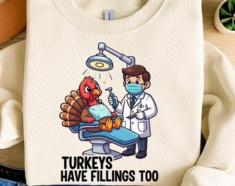 May include: Cream-colored sweatshirt with a graphic of a turkey at the dentist. The turkey is in a dental chair, and a dentist in a mask is holding dental tools. The text "TURKEYS HAVE FILLINGS TOO" is below the image.