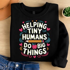 Puede incluir: Sudadera negra con el texto "Helping Tiny Humans Do Big Things" en blanco, turquesa, rosa y naranja. El diseño incluye un lápiz, corazones y una manzana. La sudadera es de cuello redondo.
