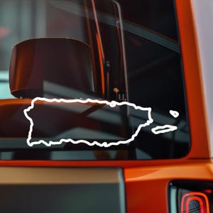 May include: A white outline of the island of Puerto Rico is displayed on a vehicle window. The image is set against a blurred background of the vehicle's interior and exterior, with an orange and gray color scheme.