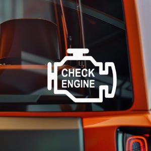 May include: White vinyl decal featuring the "Check Engine" symbol, a stylized engine outline with the words "CHECK ENGINE" inside. The decal is displayed on a vehicle's window, with an orange body visible.