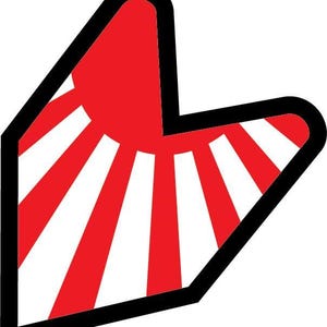 May include: A red and white Japanese beginner driver symbol, featuring a rising sun design with red rays emanating from a central red circle. The symbol is outlined in black and has a unique, angular shape.