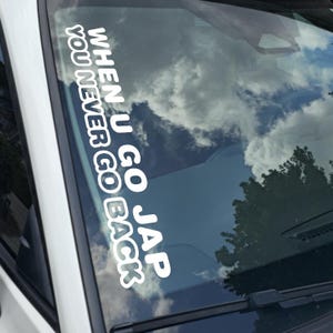 May include: White vinyl decal applied to a car windshield. The decal reads "WHEN U GO JAP YOU NEVER GO BACK" in a bold, sans-serif font. The background shows a reflection of a cloudy sky and trees.