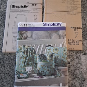 May include: A Simplicity 2911 sewing pattern envelope featuring a light blue quilted bag set with floral patterns, including a drawstring bag, a crossbody bag, and a small pouch. The set includes paper pattern instructions and a base cover piece.