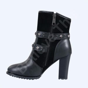 May include: Black ankle boot with a block heel. The boot features a side zip, studded straps, and a suede panel. The heel is approximately 7.6 cm high. The boot has a round toe and a textured sole.