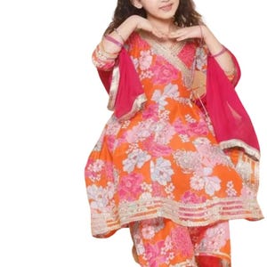 K&ouml;nnte beinhalten: Ein farbenfrohes Salwar-Kameez-Set mit einem Blumenmuster in Orange und Pink. Das Outfit besteht aus einem Wickel-Top, passenden Hosen und einem leuchtend pinkfarbenen Dupatta. Goldfarbene Verzierungen s&auml;umen die R&auml;nder des Outfits und verleihen ihm Eleganz.