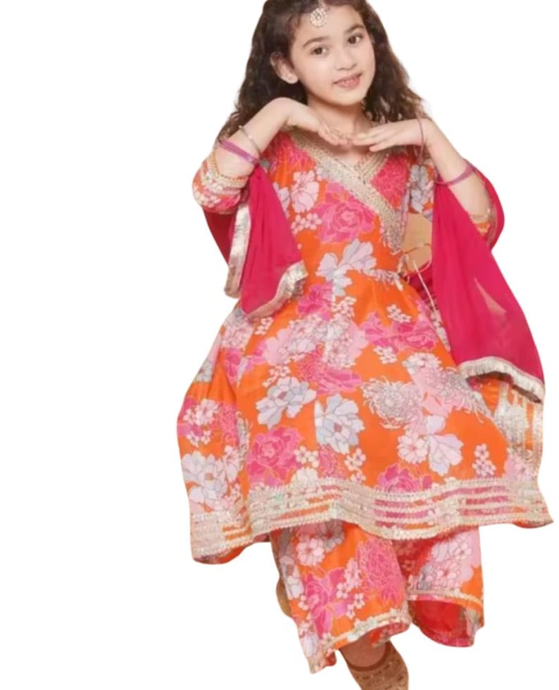 K&ouml;nnte beinhalten: Ein farbenfrohes Salwar-Kameez-Set mit einem Blumenmuster in Orange und Pink. Das Outfit besteht aus einem Wickel-Top, passenden Hosen und einem leuchtend pinkfarbenen Dupatta. Goldfarbene Verzierungen s&auml;umen die R&auml;nder des Outfits und verleihen ihm Eleganz.