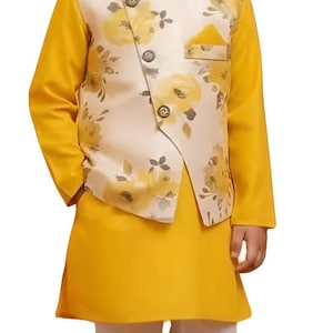 Könnte beinhalten: Ein junger Junge in einem gelben Kurta und einer weißen Hose, ergänzt durch eine Weste mit floralem Muster. Die Weste hat einen cremefarbenen Hintergrund mit gelben Blumenmustern. Das Outfit wird durch braune Schuhe abgerundet.