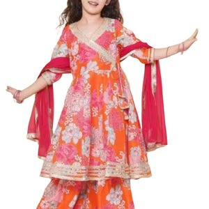 May include: A vibrant orange and pink floral print outfit for a child. The ensemble includes a wrap-style top with a V-neck, matching palazzo pants, and a flowing red scarf. The outfit is trimmed with gold accents.