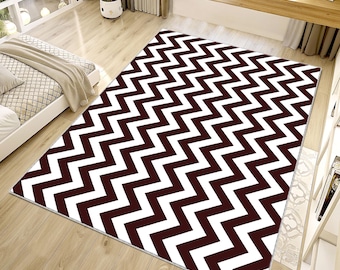 Puede incluir: Una alfombra rectangular grande con un llamativo patrón en zigzag en blanco y marrón oscuro. La alfombra está colocada sobre un suelo de madera, creando un contraste visual audaz. La alfombra es un elemento decorativo para un espacio habitable, de unos 200 cm x 300 cm.