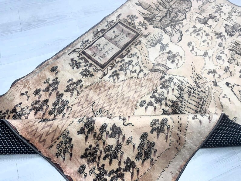 Puede incluir: Textil beige y negro con tem&aacute;tica de mapa con ilustraciones y texto de la serie Harry Potter. El mapa incluye el texto "The Wizarding World of Harry Potter" y un borde negro punteado.