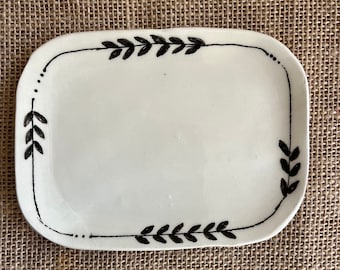 May include: A white ceramic rectangular dish with a black hand-painted border of leaves.