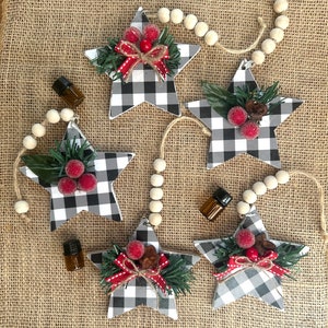 May include: Five star-shaped ornaments with a black and white checkered pattern, decorated with red berries, greenery, and a red and white ribbon. Each ornament hangs from a string of wooden beads. Small brown glass bottles are also present.