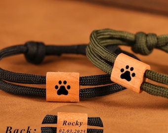 May include: Two bracelets with a wooden accent featuring a black paw print. One bracelet is black, the other is olive green. The back of one bracelet has the name "Rocky" and the date "02.03.2025" engraved.